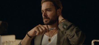 Movie still from “A Deadly Invitation” (2023), directed by J.M Cravioto – A man with a beard is holding a pen in his mouth; Close Up shot, Low angle