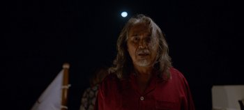 Movie still from “A Deadly Invitation” (2023), directed by J.M Cravioto – An older man with long hair and a red shirt; Close Up shot, Over the shoulder angle