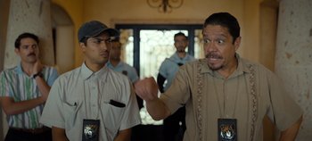 Movie still from “A Deadly Invitation” (2023), directed by J.M Cravioto – A man in a tan shirt is talking to two other men; Medium shot, Over the shoulder angle