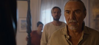 Movie still from “A Deadly Invitation” (2023), directed by J.M Cravioto – A man and a woman standing next to another man in front of a window; Close Up shot, Over the shoulder angle