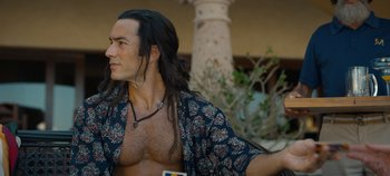 Movie still from “A Deadly Invitation” (2023), directed by J.M Cravioto – A man with long black hair is wearing a shirt; Close Up shot, Over the shoulder angle