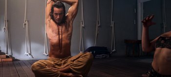 Movie still from “A Deadly Invitation” (2023), directed by J.M Cravioto – A man sitting on the ground doing a yoga pose; Medium shot, Low angle