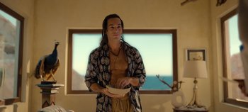 Movie still from “A Deadly Invitation” (2023), directed by J.M Cravioto – A man with long brown hair holding a bowl in front of a window; Medium shot, Over the shoulder angle