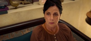 Movie still from “A Deadly Invitation” (2023), directed by J.M Cravioto – An older woman wearing a brown shirt and a necklace; Close Up shot, High angle