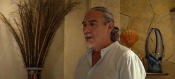Movie still from “A Deadly Invitation” (2023), directed by J.M Cravioto – An older man with long gray hair wearing a white shirt; Close Up shot, Over the shoulder angle