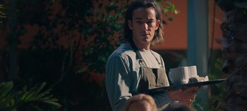 Movie still from “A Deadly Invitation” (2023), directed by J.M Cravioto – A man in an apron is holding a book; Medium shot, Low angle