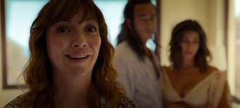 Movie still from “A Deadly Invitation” (2023), directed by J.M Cravioto – A woman smiles while standing in front of two other people; Close Up shot, Over the shoulder angle