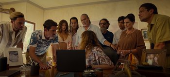 Movie still from “A Deadly Invitation” (2023), directed by J.M Cravioto – A group of people gathered around a woman looking at a laptop computer; Medium shot, High angle