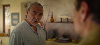 Movie still from “A Deadly Invitation” (2023), directed by J.M Cravioto – An older man standing in front of a wall with vases on it; Close Up shot, Over the shoulder angle