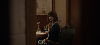 Movie still from “A Deadly Invitation” (2023), directed by J.M Cravioto – A woman sitting in a chair in front of a desk; Medium shot, High angle