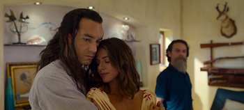 Movie still from “A Deadly Invitation” (2023), directed by J.M Cravioto – A man and a woman embracing each other in front of another man in a room; Close Up shot, Over the shoulder angle