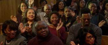 Movie still from “A Fall from Grace” (2020), directed by Tyler Perry – A group of people sitting and standing in a room; Medium shot, High angle