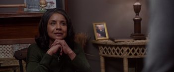 Movie still from “A Fall from Grace” (2020), directed by Tyler Perry – A woman sitting in front of a table with a picture of a man; Close Up shot, Over the shoulder angle