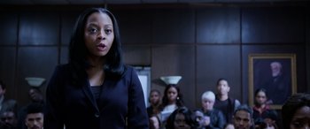 Movie still from “A Fall from Grace” (2020), directed by Tyler Perry – A woman standing in front of a group of people; Medium shot, Over the shoulder angle