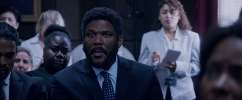 Movie still from “A Fall from Grace” (2020), directed by Tyler Perry – A man in a suit and tie looking at the camera; Medium shot, Over the shoulder angle