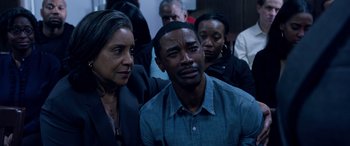 Movie still from “A Fall from Grace” (2020), directed by Tyler Perry – A man and a woman looking sad in front of a group of people; Medium shot, High angle