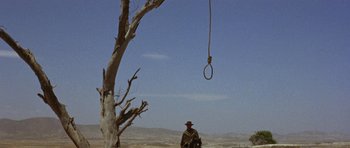 Movie still from “A Fistful of Dollars” (1964), directed by Sergio Leone – A man sitting in front of a rope hanging from a tree; Wide shot, Low angle