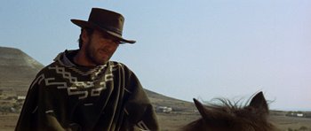 Movie still from “A Fistful of Dollars” (1964), directed by Sergio Leone – A man wearing a hat and a poncho rides a horse; Medium shot, Low angle