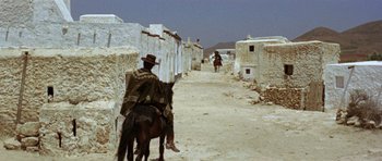 Movie still from “A Fistful of Dollars” (1964), directed by Sergio Leone – A man riding a horse down a dirt road; Wide shot, High angle