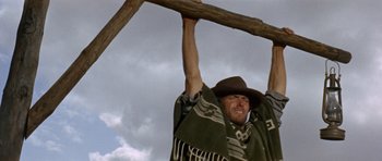 Movie still from “A Fistful of Dollars” (1964), directed by Sergio Leone – A man hanging from a wooden stick in the air; Medium shot, Low angle