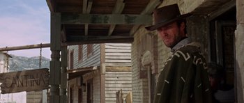 Movie still from “A Fistful of Dollars” (1964), directed by Sergio Leone – A man wearing a cowboy hat standing in an alley way; Medium shot, Low angle