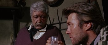 Movie still from “A Fistful of Dollars” (1964), directed by Sergio Leone – A man holding a glass in front of another man; Close Up shot, Over the shoulder angle
