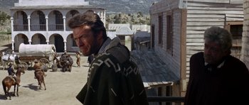 Movie still from “A Fistful of Dollars” (1964), directed by Sergio Leone – A man with a beard is standing in the middle of a street; Medium shot, Over the shoulder angle
