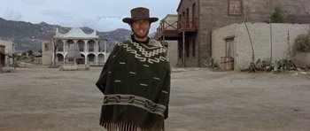 Movie still from “A Fistful of Dollars” (1964), directed by Sergio Leone – A man wearing a hat and a poncho in the middle of an empty street; Wide shot, Low angle