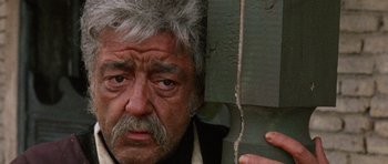 Movie still from “A Fistful of Dollars” (1964), directed by Sergio Leone – An older man with a beard and a mustache looking sad; Close Up shot, Low angle