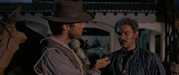 Movie still from “A Fistful of Dollars” (1964), directed by Sergio Leone – A man in a cowboy hat is talking to another man; Close Up shot, Over the shoulder angle