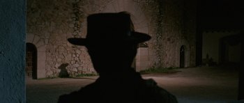 Movie still from “A Fistful of Dollars” (1964), directed by Sergio Leone – A man wearing a black hat in front of an archway; Close Up shot, Over the shoulder angle