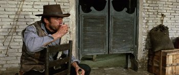 Movie still from “A Fistful of Dollars” (1964), directed by Sergio Leone – A man sitting on a bench eating food; Medium shot, Low angle