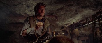 Movie still from “A Fistful of Dollars” (1964), directed by Sergio Leone – A man sitting at a table in a cave; Close Up shot, Low angle