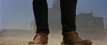 Movie still from “A Fistful of Dollars” (1964), directed by Sergio Leone – A person wearing brown shoes standing in the dirt; Wide shot, Low angle