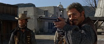 Movie still from “A Fistful of Dollars” (1964), directed by Sergio Leone – A man is aiming a gun at a building; Medium shot, Low angle