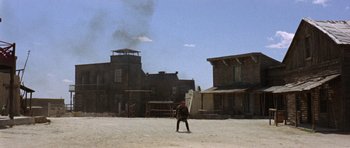 Movie still from “A Fistful of Dollars” (1964), directed by Sergio Leone – A man standing in a dirt field near buildings; Extreme Wide shot, Low angle