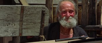 Movie still from “A Fistful of Dollars” (1964), directed by Sergio Leone – An old man sitting at a table holding a piece of wood in front of him; Close Up shot, Low angle