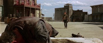 Movie still from “A Fistful of Dollars” (1964), directed by Sergio Leone – A man walking down a street near a building; Wide shot, Over the shoulder angle