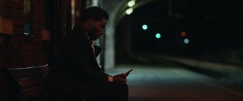 Movie still from “A Good Person” (2023), directed by Zach Braff – A man sitting on the ground looking at his cell phone; Medium shot, Low angle