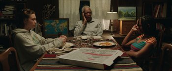 Movie still from “A Good Person” (2023), directed by Zach Braff – An older man sitting at a table with a plate of pizza; Medium shot, High angle
