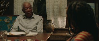 Movie still from “A Good Person” (2023), directed by Zach Braff – An older man sitting at a table in front of a vase; Medium shot, Over the shoulder angle