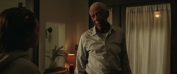 Movie still from “A Good Person” (2023), directed by Zach Braff – An older man standing in front of a table; Medium shot, Low angle