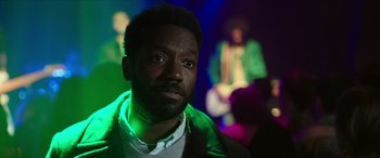 Movie still from “A Good Person” (2023), directed by Zach Braff – A person wearing a jacket with lights in the background; Close Up shot, Over the shoulder angle