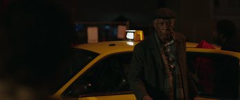 Movie still from “A Good Person” (2023), directed by Zach Braff – An older man standing next to a yellow taxi cab at night; Medium shot, Low angle