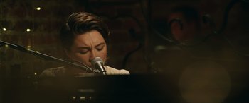 Movie still from “A Good Person” (2023), directed by Zach Braff – A person sitting at a piano with a microphone; Close Up shot, Over the shoulder angle