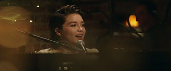 Movie still from “A Good Person” (2023), directed by Zach Braff – A woman with short black hair sitting in front of a microphone; Close Up shot, Over the shoulder angle