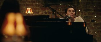Movie still from “A Good Person” (2023), directed by Zach Braff – A person sitting at a piano with a microphone; Medium shot, Over the shoulder angle