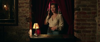 Movie still from “A Good Person” (2023), directed by Zach Braff – A woman standing in front of a mirror talking on the phone; Medium shot, Low angle