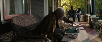 Movie still from “A Good Person” (2023), directed by Zach Braff – An older man sitting on a chair on a porch; Medium shot, Over the shoulder angle