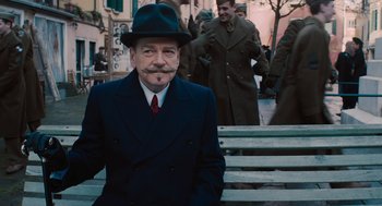 Movie still from “A Haunting in Venice” (2023), directed by Kenneth Branagh – A man in a hat and a suit is sitting on some steps; Medium shot, Over the shoulder angle